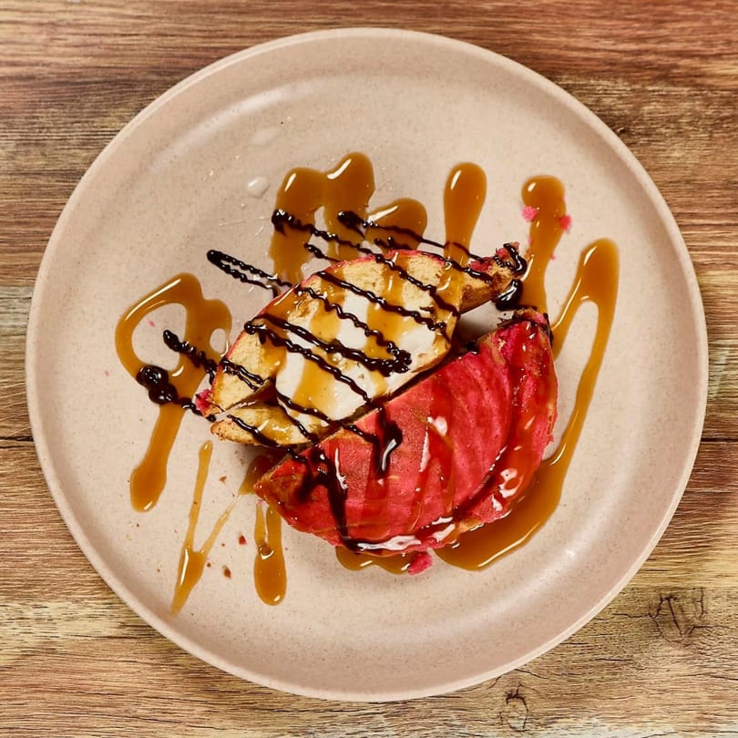 Two slices of cake, one red and one white, drizzled with caramel and chocolate on a plate.