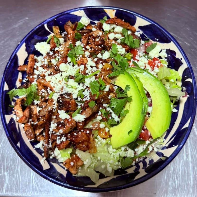 Mexican salad with grilled chicken, crumbled cheese, cilantro, and avocado slices in a blue and white bowl.