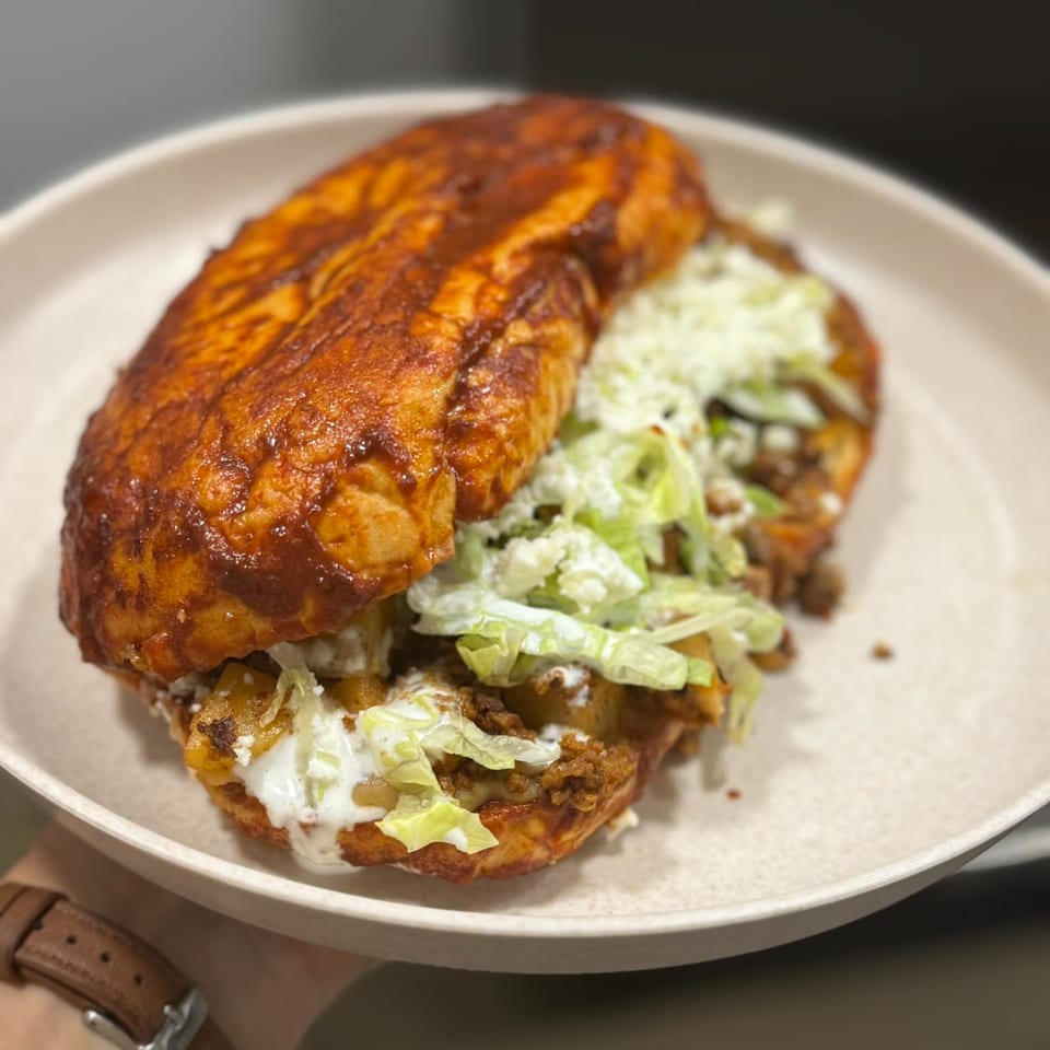 A Mexican pambazo sandwich, filled with meat and lettuce, drizzled with cream, on a white plate.