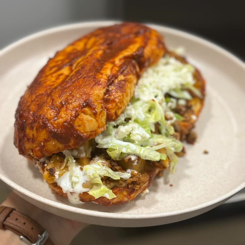 A Mexican pambazo sandwich, filled with meat and lettuce, drizzled with cream, on a white plate.