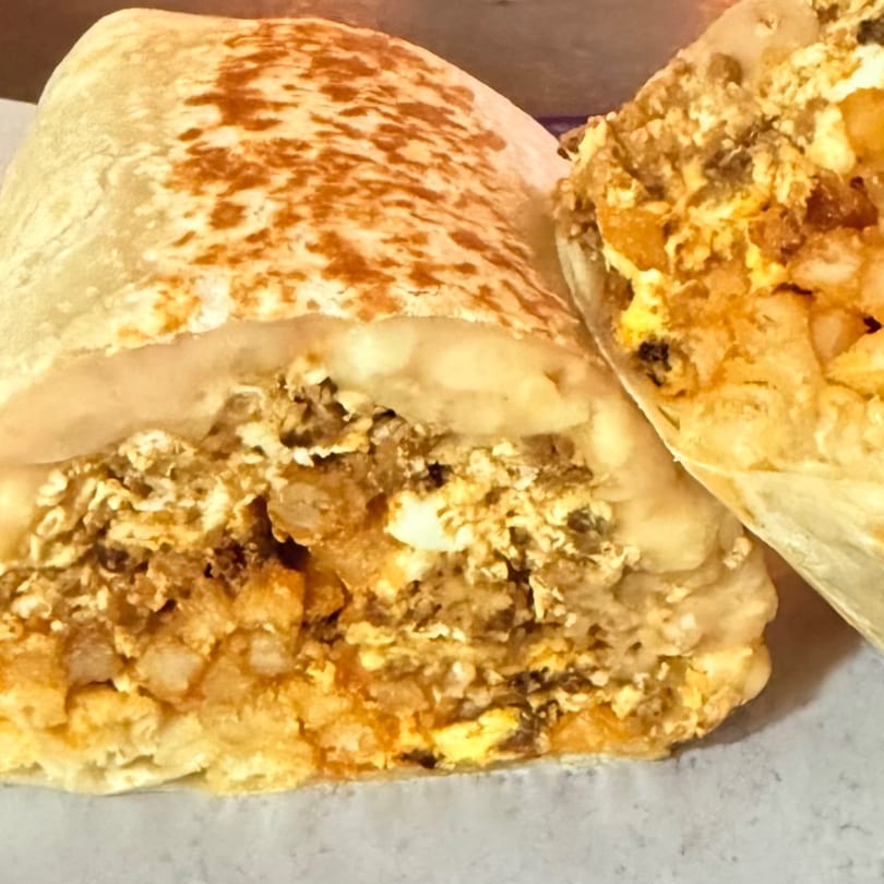 A close-up of a La Gruta Signature Cuisine burrito, cut in half, revealing a savory filling.