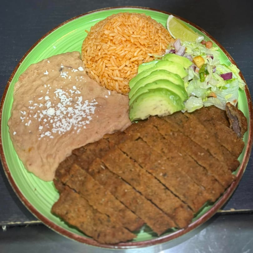 La Gruta's Mexican dish with sliced meat, rice, refried beans, avocado, and salad on a green plate.
